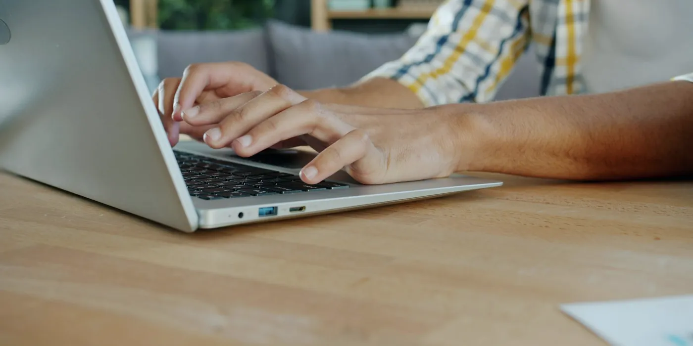 Mains sur le clavier d'un ordinateur portable posé sur une table en bois