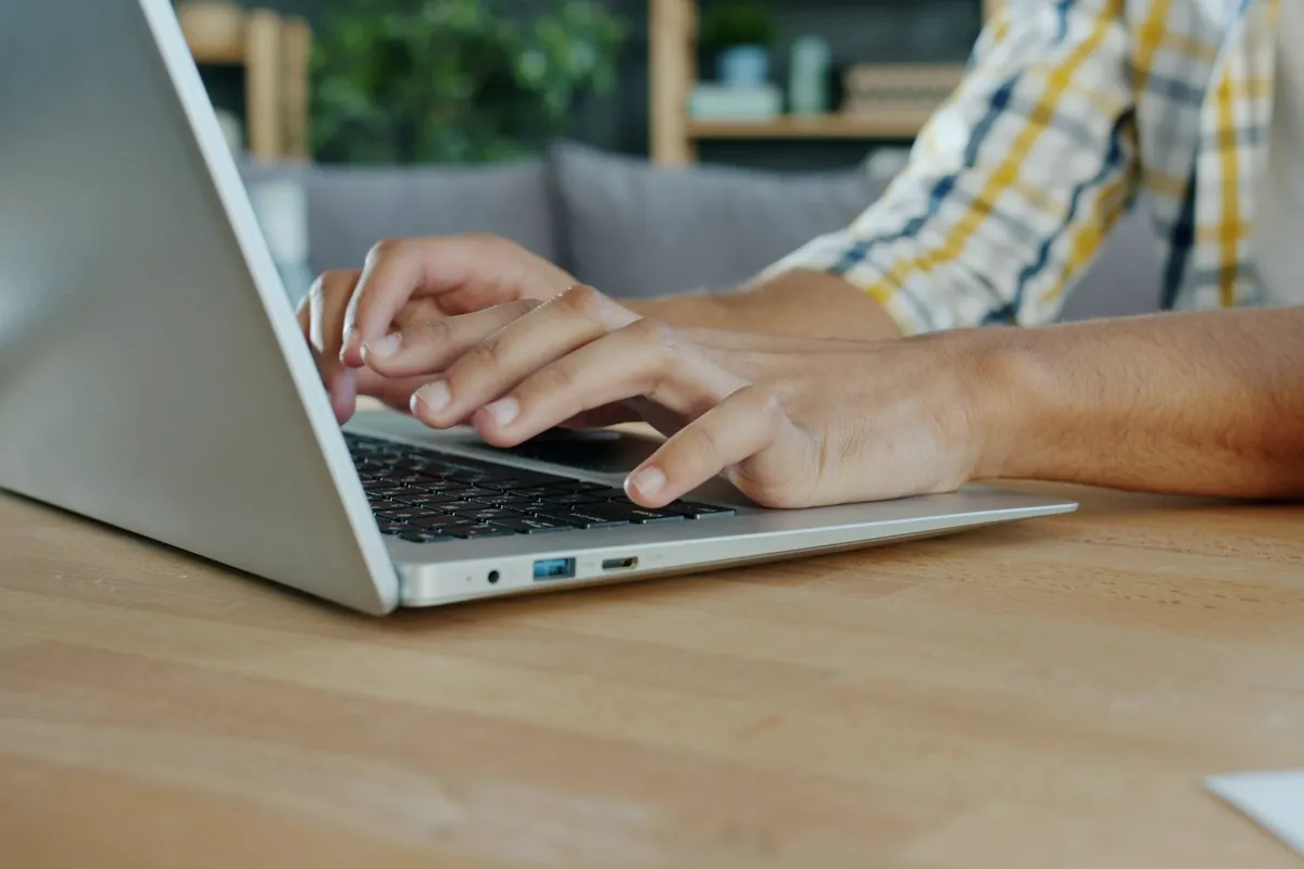 Mains sur le clavier d'un ordinateur portable posé sur une table en bois